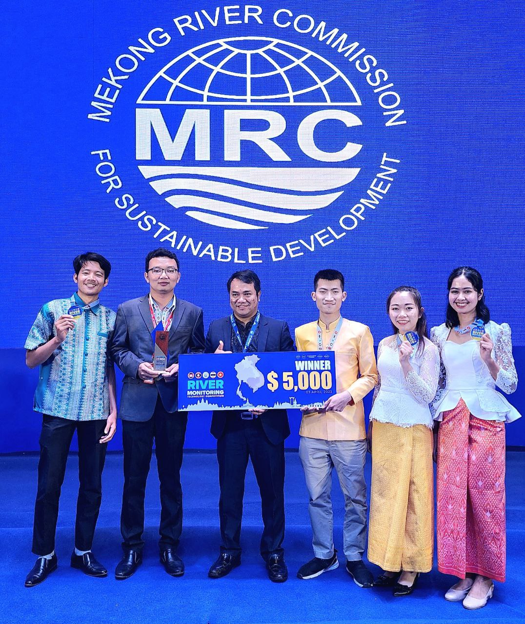 Six people posing with a River Monitoring Technology Competition winner sign at a Mekong River Commission event